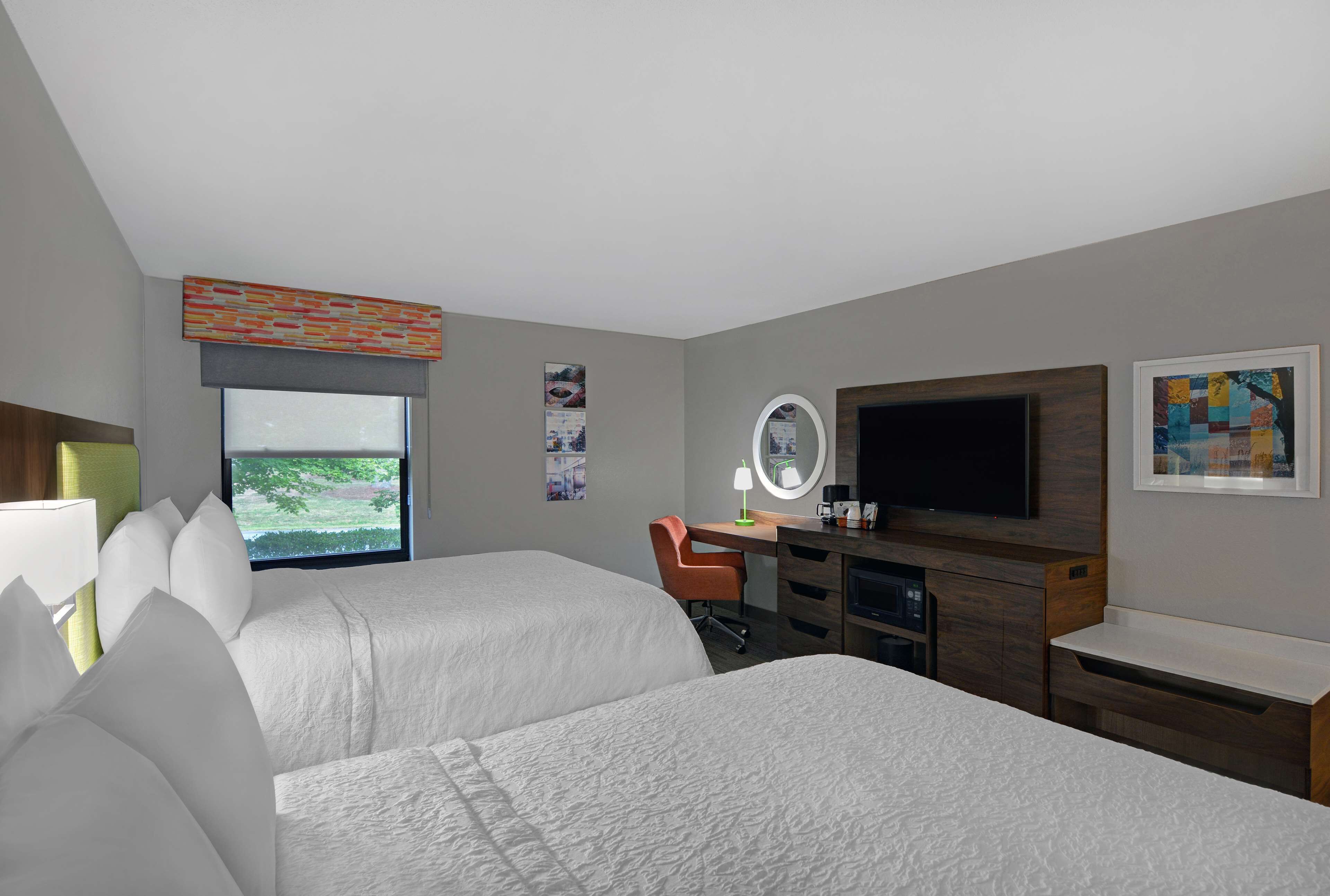 Een hotelkamer met twee bedden, een bureau met een computer, een televisie en een raam met uitzicht op groen.