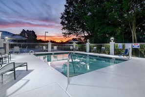 A swimming pool with a sunset view, surrounded by a fence, chairs, and umbrellas.