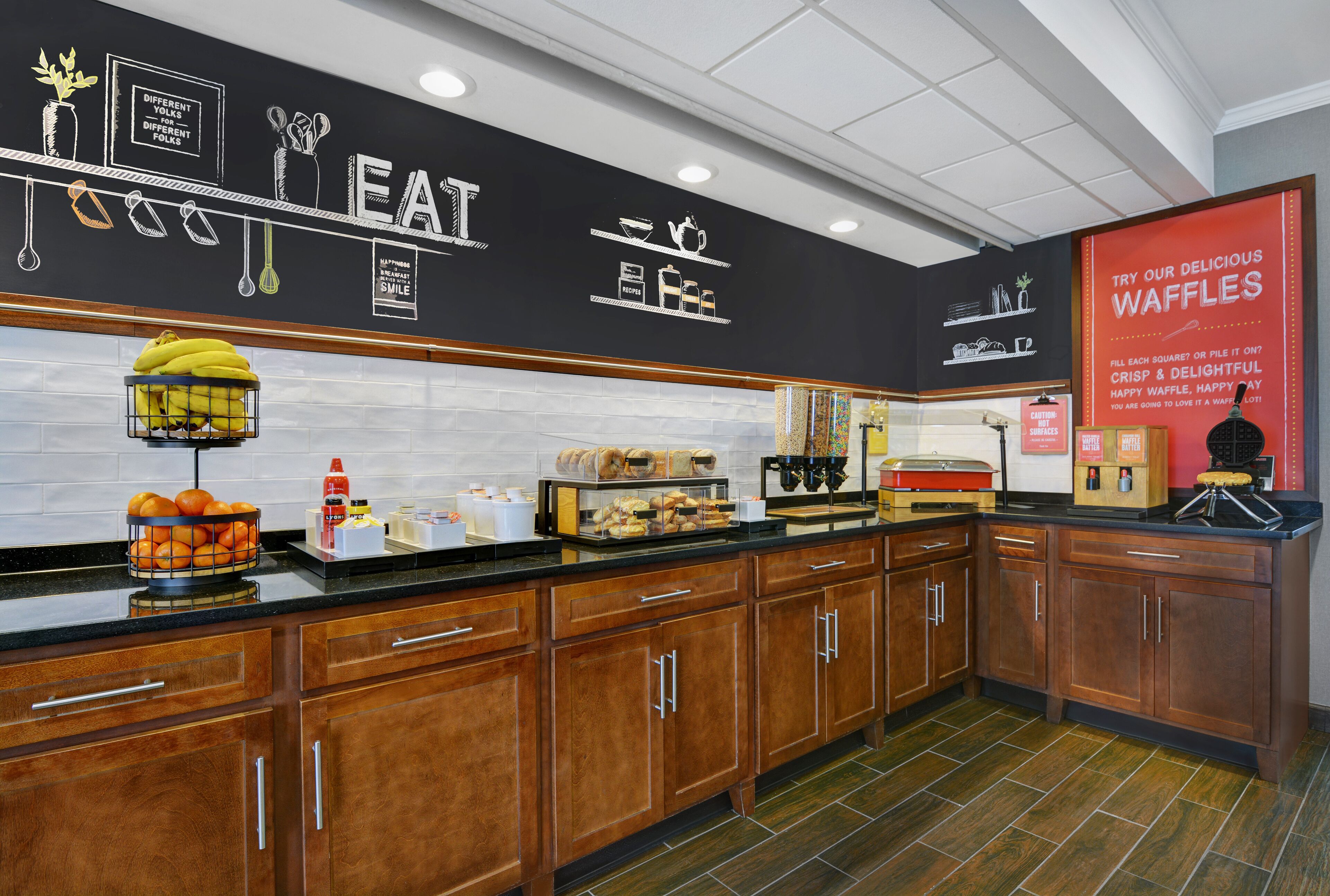 A kitchen with wooden cabinets, a black backsplash, and a red sign advertising waffles.