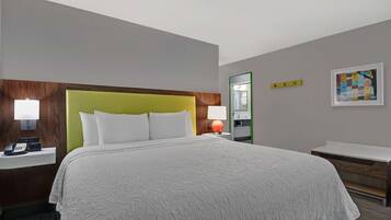 Habitación de hotel con una cama grande, una mesita de noche con lámpara, teléfono, espejo y una obra de arte enmarcada en la pared.