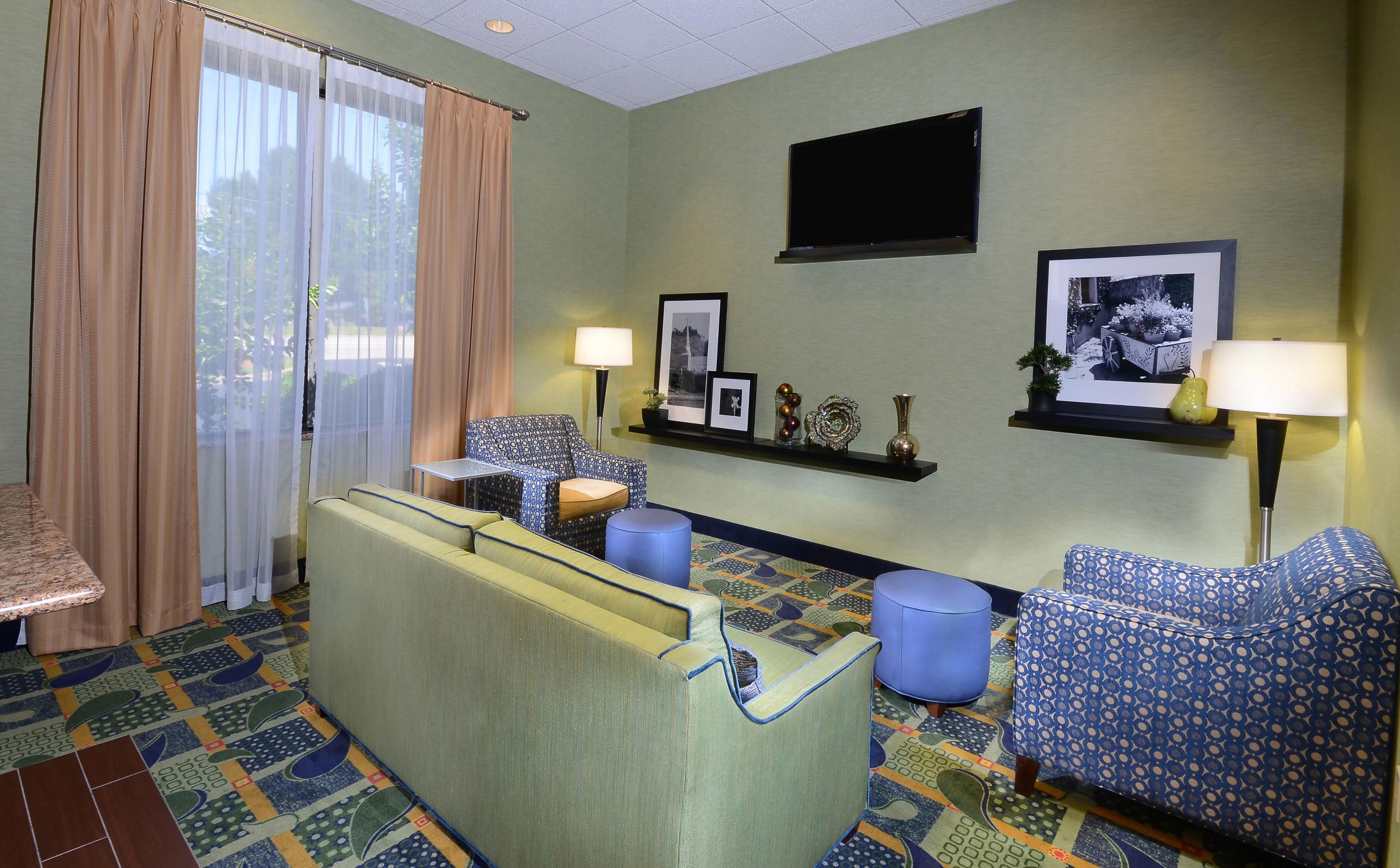 Habitación de hotel con sofá, sillones, una mesita, televisor y alfombra estampada.