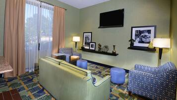 Habitación de hotel con sofá, sillones, una mesita, televisor y alfombra estampada.