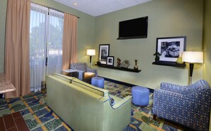 Habitación de hotel con sofá, sillones, una mesita, televisor y alfombra estampada.