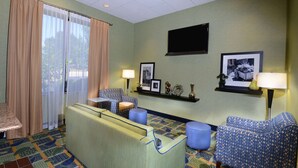 Habitación de hotel con sofá, sillones, una mesita y televisor montado en la pared.
