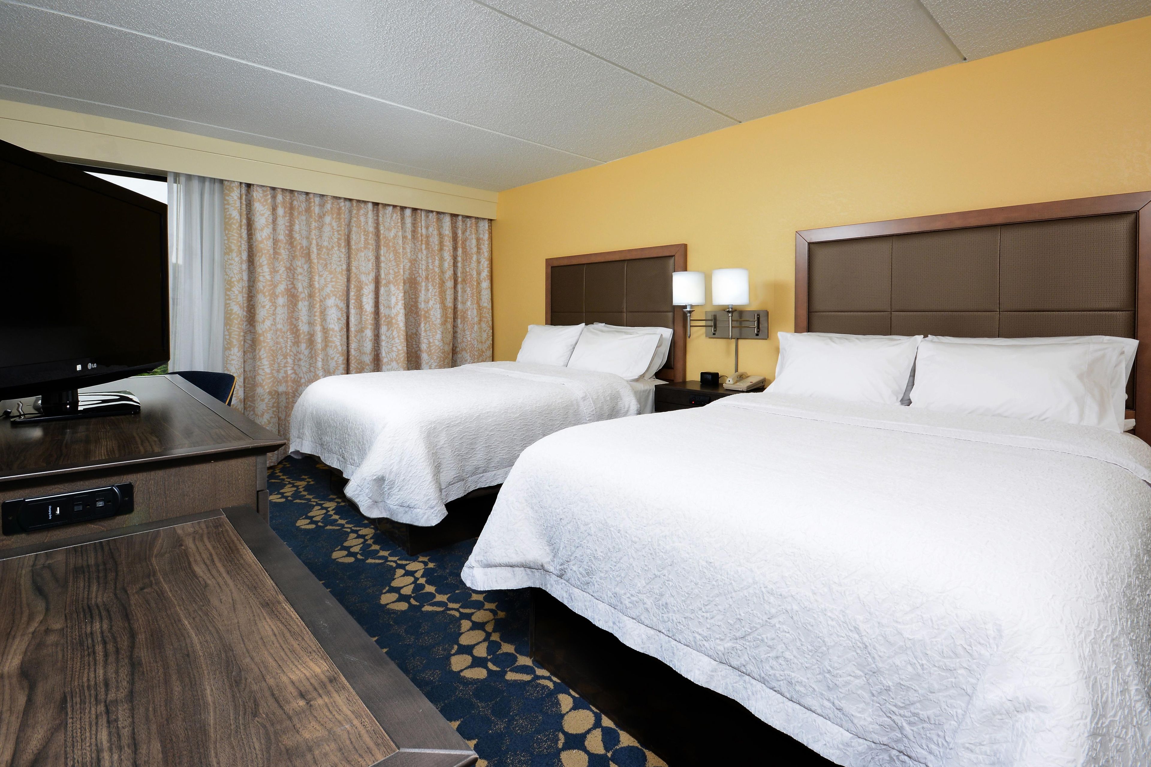 A hotel room with two beds, a desk, a television, and a carpeted floor.