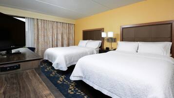A hotel room with two beds, a desk, a television, and a carpeted floor.