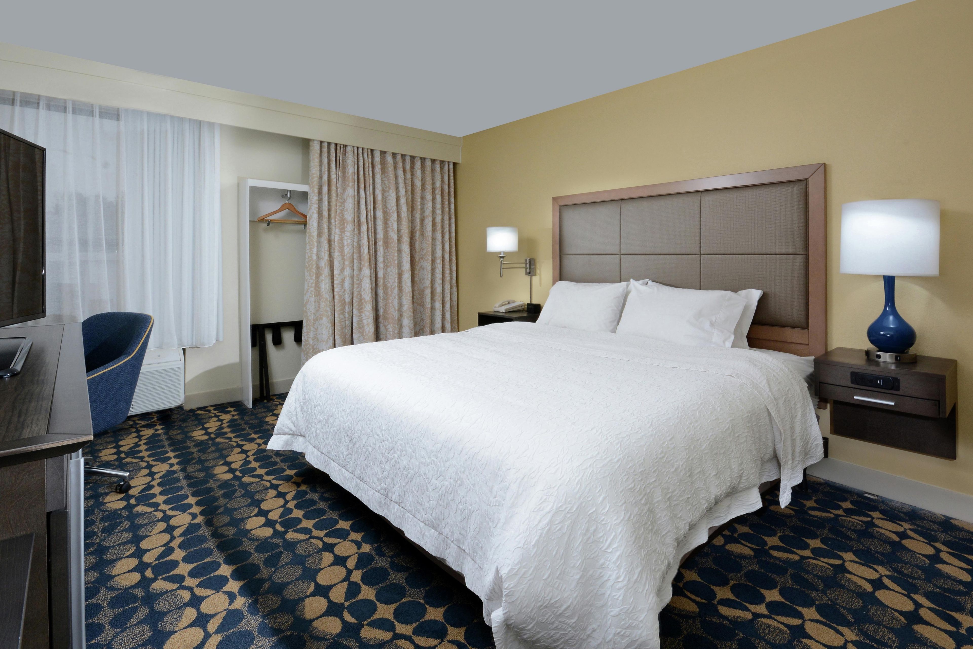 Une chambre d’hôtel avec un grand lit, un bureau avec une chaise, une table de chevet avec une lampe et une armoire.