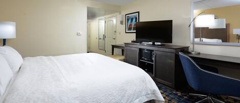 Une chambre d’hôtel avec un lit, un bureau, une télévision et un miroir dans la salle de bain.