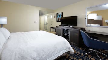Habitación de hotel con una cama grande, un escritorio con computadora, televisor de pantalla plana, un espejo y una puerta que da a otra habitación.