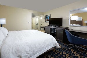 Camera d'albergo con un letto grande, una scrivania con un computer, una TV a schermo piatto, uno specchio e una porta che dà su un'altra stanza.