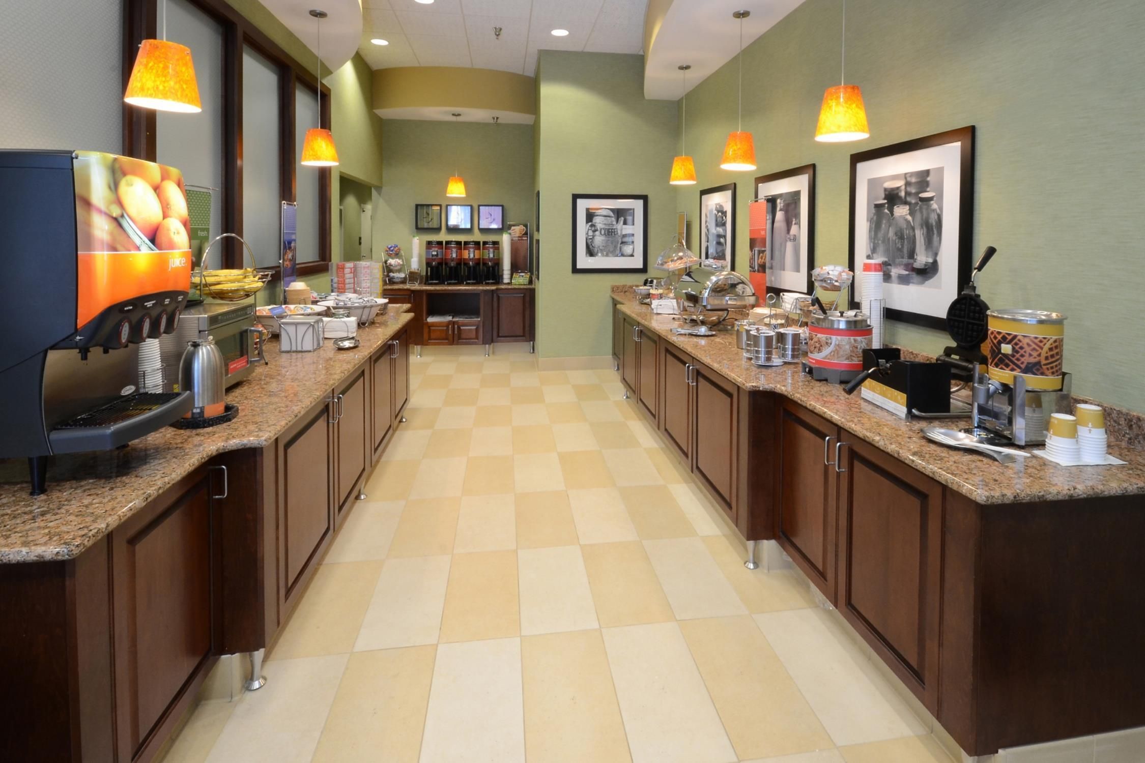 A hotel breakfast area with a self-serve coffee station, juice dispenser, and various food options.