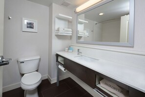 Un baño moderno con inodoro, lavamanos y espejo. Hay repisas con toallas y un secador de pelo.