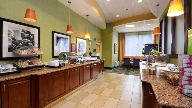 Zona de desayuno de hotel con una barra larga, exhibición de alimentos y área de estar.