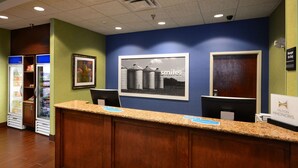 Zona de recepción de un hotel con un mostrador de madera, un cuadro enmarcado en la pared y un refrigerador con bebidas.