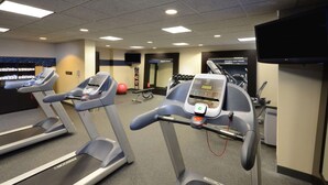Un gimnasio con cintas de correr, pesas y una pantalla de televisión mostrando un anuncio.