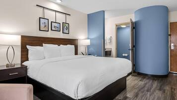 Une chambre d’hôtel avec un grand lit, des tables de chevet, un bureau, une chaise, une armoire et une salle de bain visible à travers une porte ouverte.