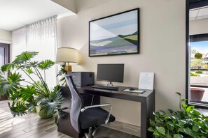 A hotel room with a desk, computer, chair, lamp, and a window with a view of buildings. - Sleep Inn Hanes Mall (Winston-Salem)