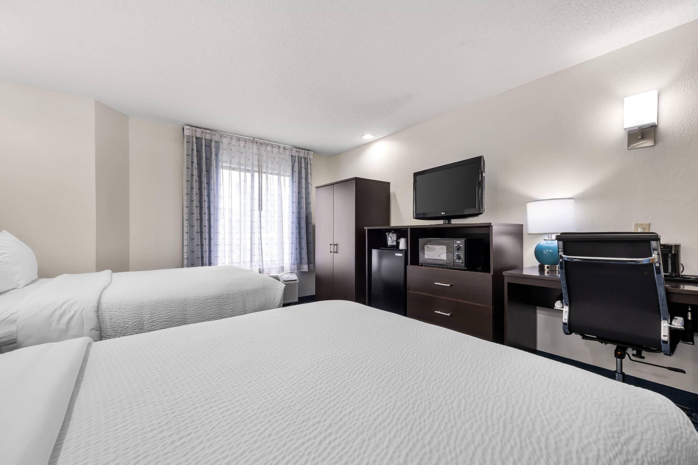 Een hotelkamer met twee bedden, een flatscreen televisie, een magnetron, een bureau met lamp en een minibar.