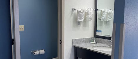 A bathroom with a toilet, a sink with a mirror, and towels hanging on a rack.