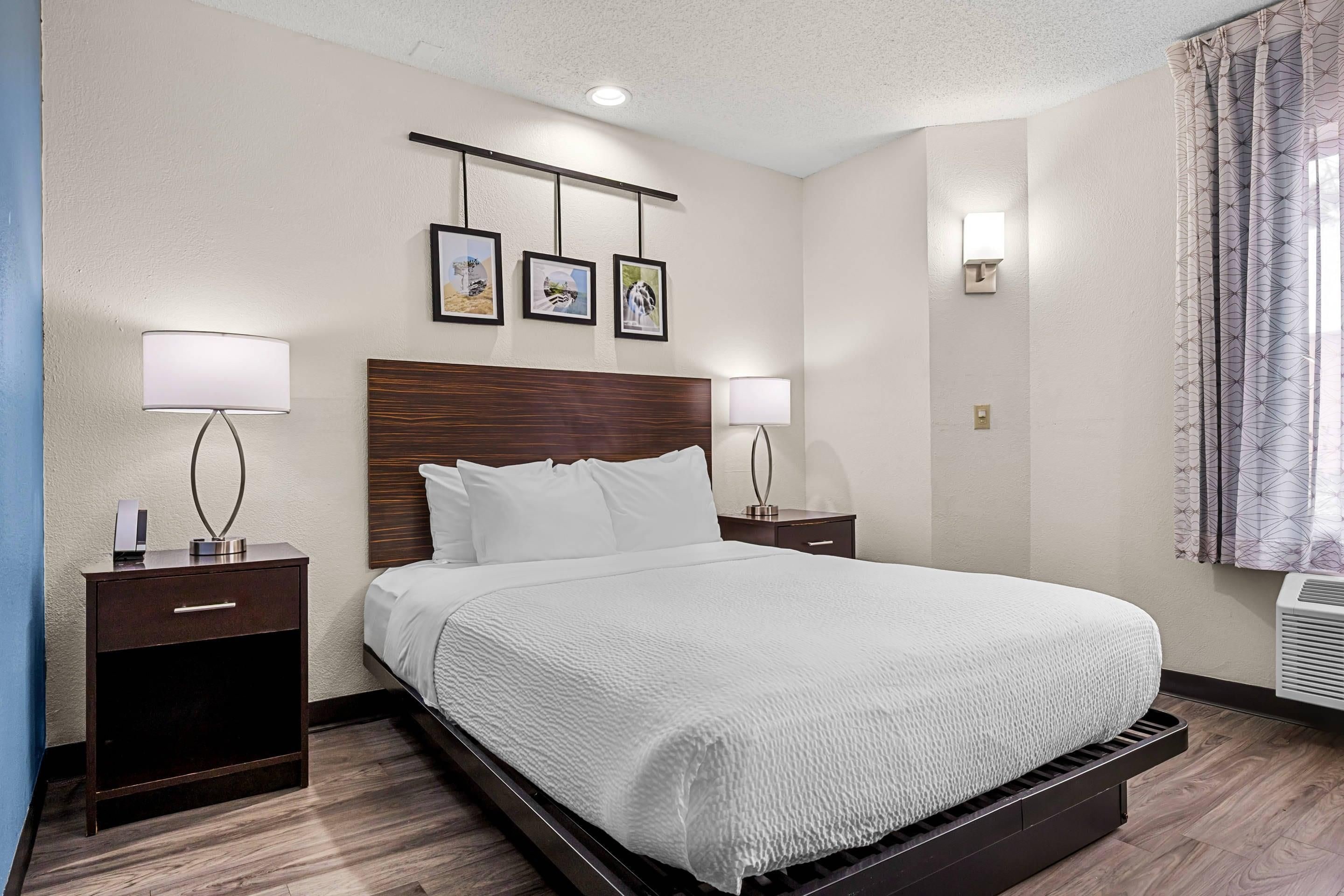 Una habitación de hotel con una cama grande, dos mesitas de noche con lámparas, un cabecero y tres cuadros enmarcados en la pared.