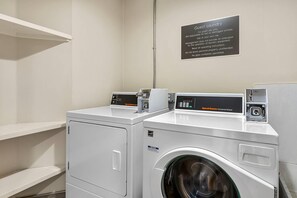 A guest laundry area with two Speed Queen Commercial Washers, a notice sign, and a shelf. - Sleep Inn Hanes Mall (Winston-Salem)