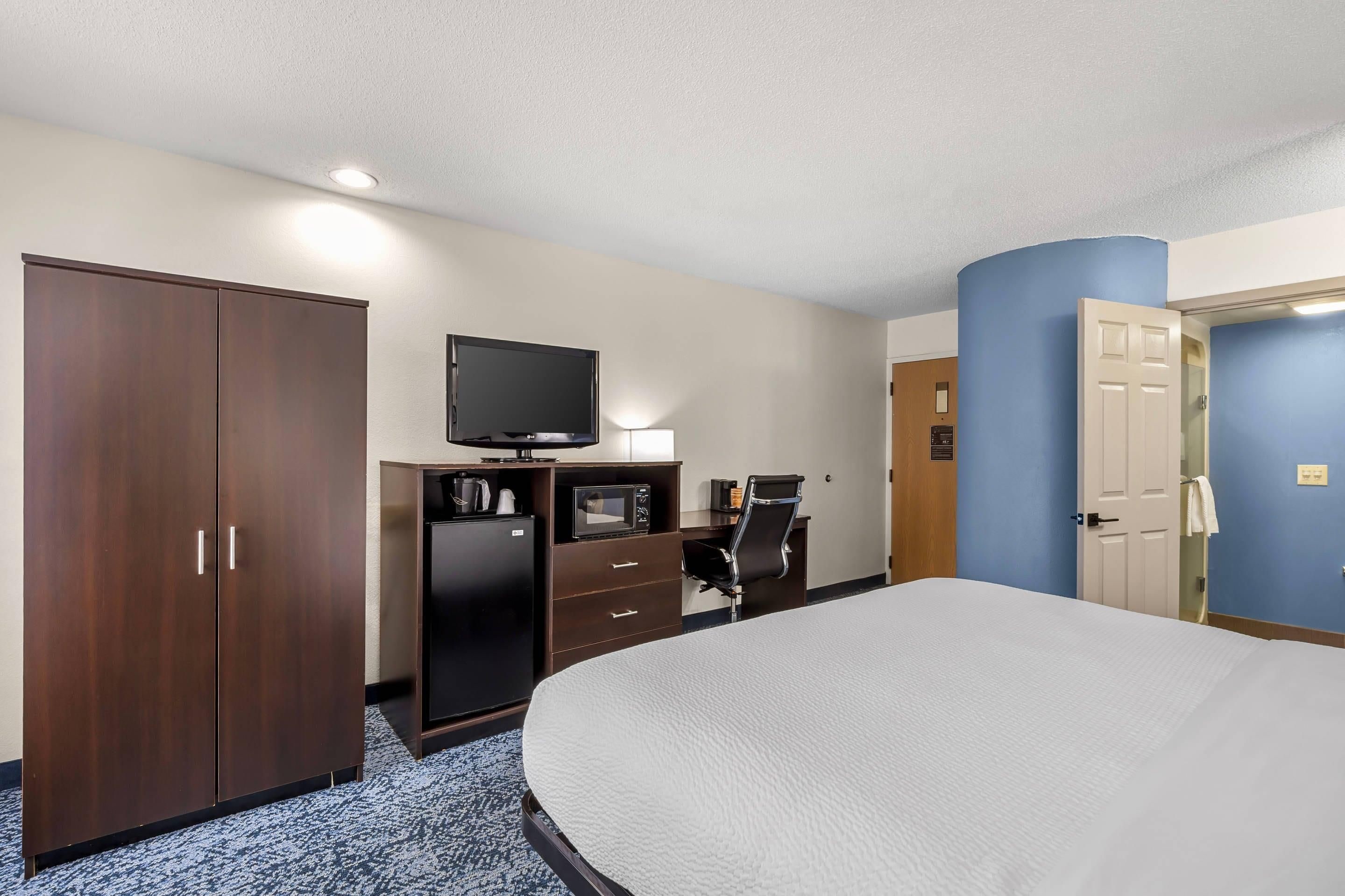 A hotel room with a bed, wardrobe, desk with a flat-screen TV, and a chair.