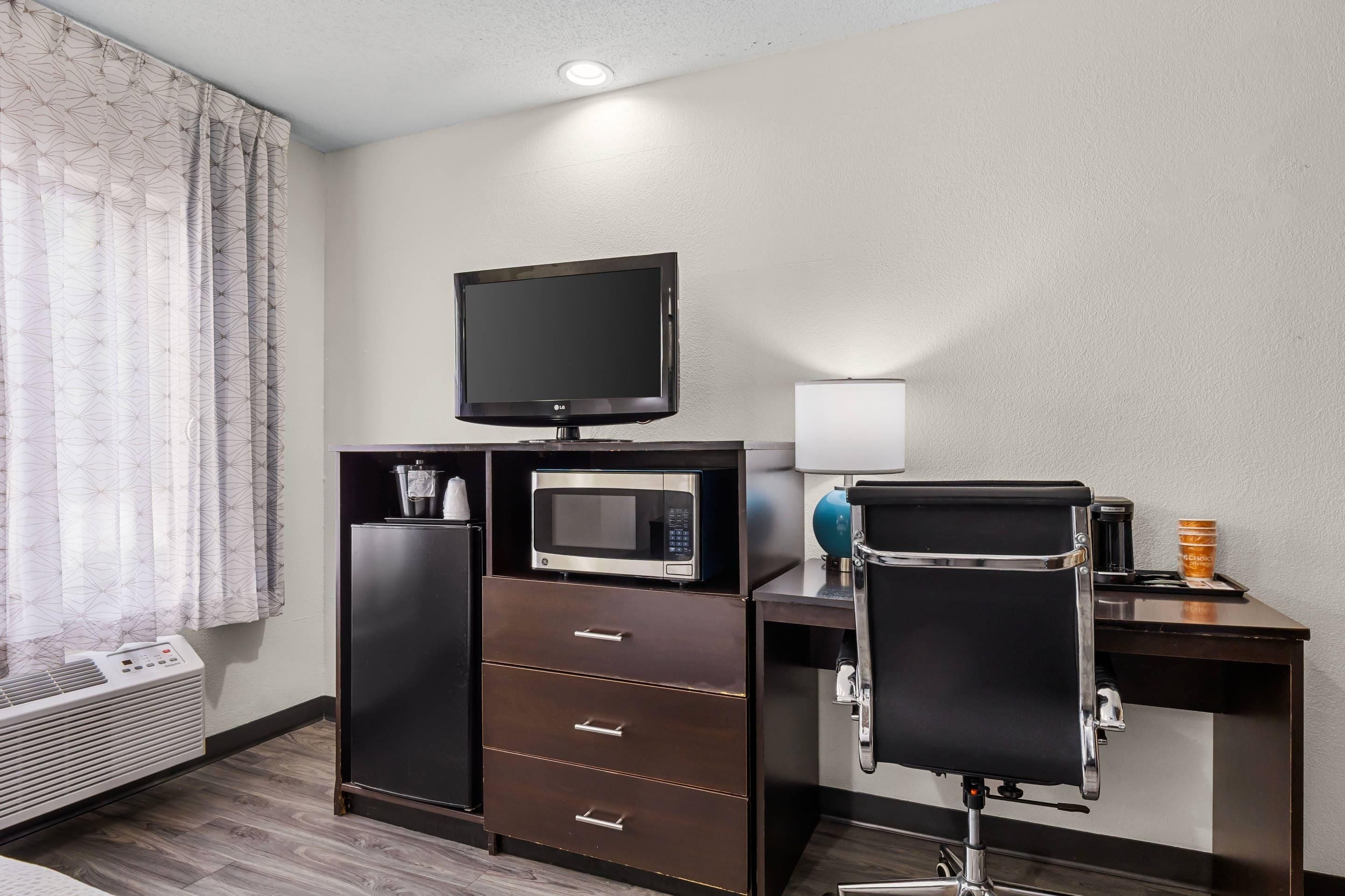 Habitación de hotel con televisión de pantalla plana, microondas, refrigerador minibar, escritorio con silla y calentador.