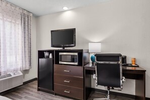 A hotel room with a flat-screen TV, a microwave, a mini-fridge, a desk with a chair, and a heater. - Sleep Inn Hanes Mall (Winston-Salem)