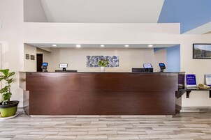 Un mostrador de recepción con encimera de madera, un cartel de bienvenida y un quiosco digital.