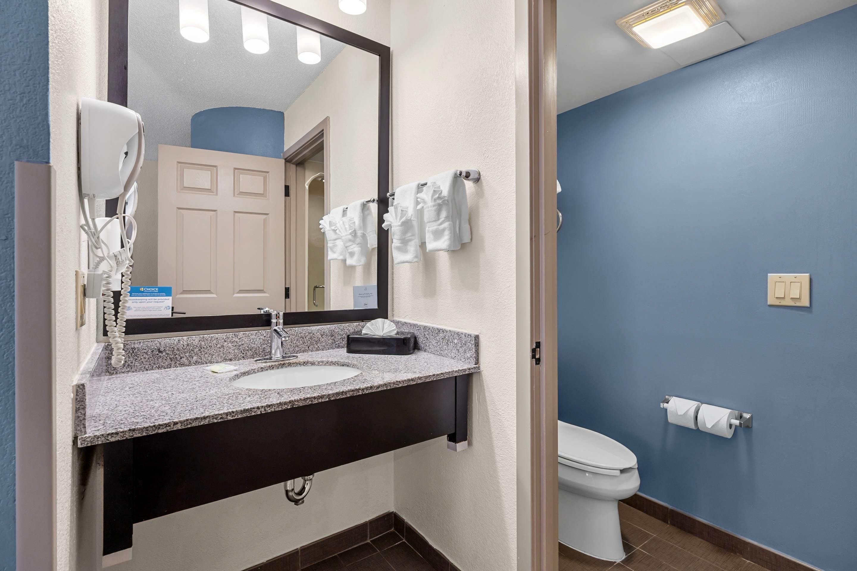 Un baño con lavamanos, espejo, toallero y retrete.