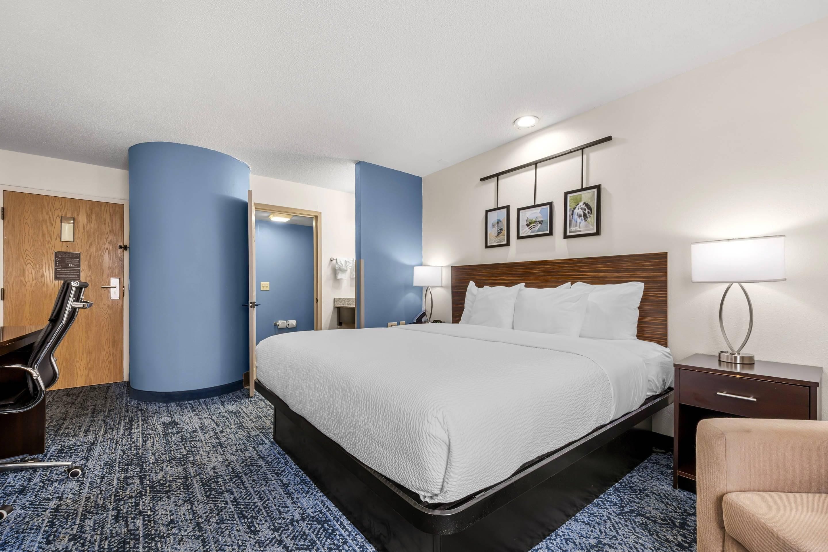 A hotel room with a large bed, a desk, a chair, and a bathroom visible through an open door.