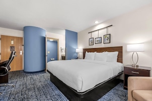 Habitación de hotel con una cama grande, un escritorio, una silla y un baño visible a través de una puerta abierta.