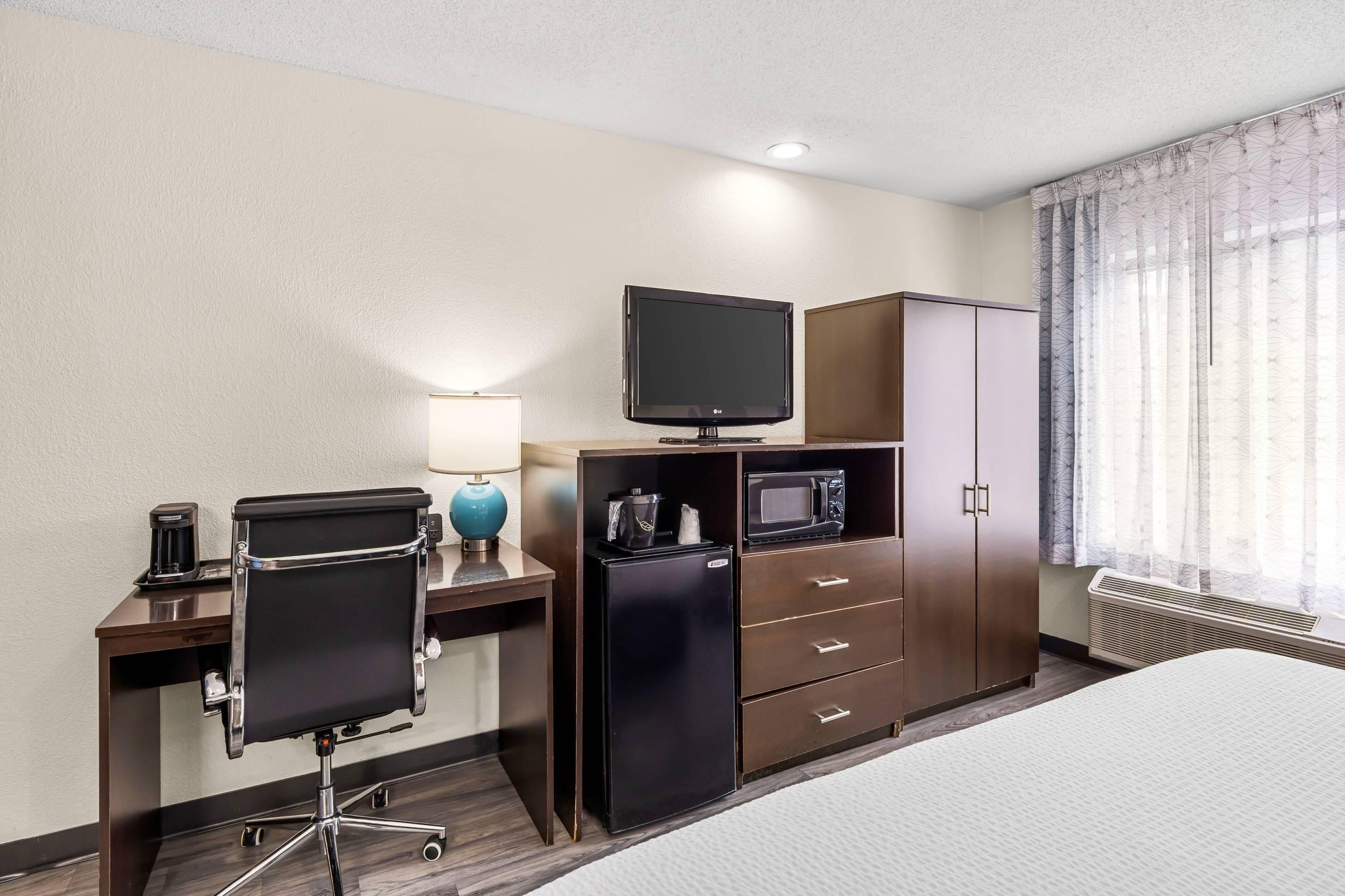 Habitación de hotel con cama, escritorio con computadora, televisor, microondas, refrigerador y armario.