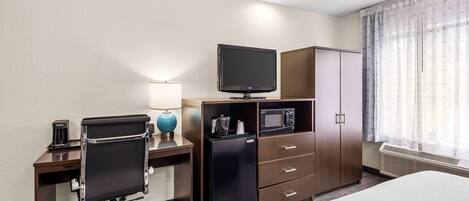 Une chambre d’hôtel comprenant un lit, un bureau avec un ordinateur, une télévision, un four à micro-ondes, un réfrigérateur et une armoire.