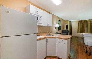 Cocina compacta con refrigerador, microondas y pileta. Se observa un pequeño comedor con una silla y una mesa.