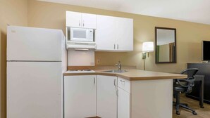 Una cocina compacta con armarios blancos, microondas, refrigerador, pileta y un pequeño escritorio con silla.