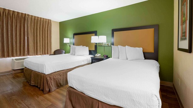 Habitación de hotel con dos camas, un ventanal con cortinas, un escritorio con lámpara y un cuadro en la pared.