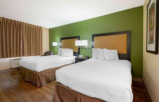 Habitación de hotel con dos camas, un ventanal con cortinas, un escritorio con lámpara y un cuadro en la pared.