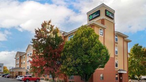Un hotel Stay America con fachada color beige, múltiples ventanas y un estacionamiento con automóviles.