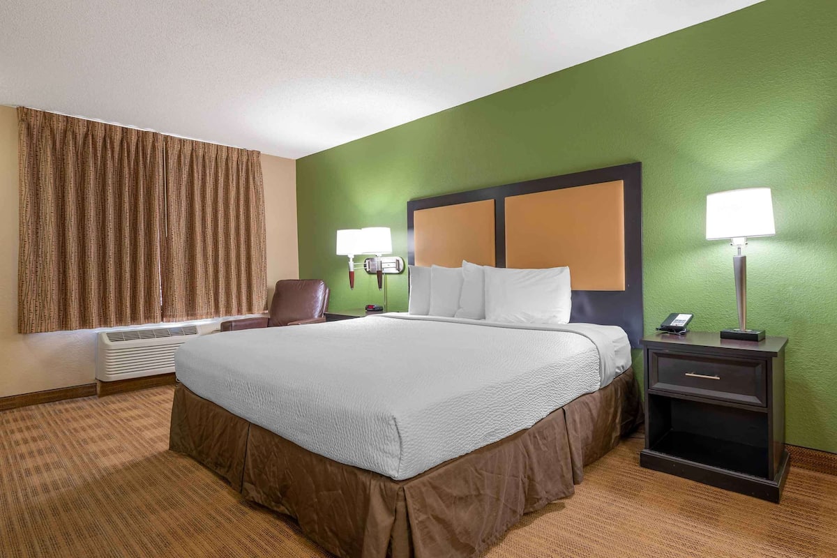 A hotel room with a large bed, two bedside lamps, a chair, a nightstand, and a wall-mounted heater.