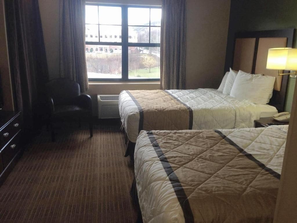 A hotel room with two beds, a desk, a chair, a window with a view, and a lamp.