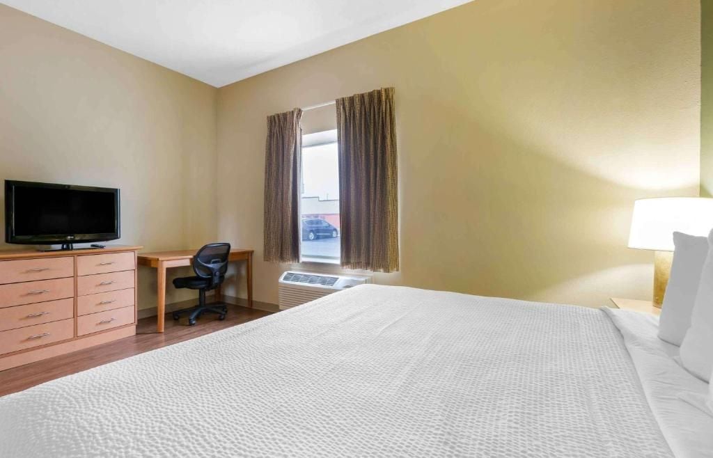 A hotel room with a bed, a desk, a chair, a television, and a window with curtains.
