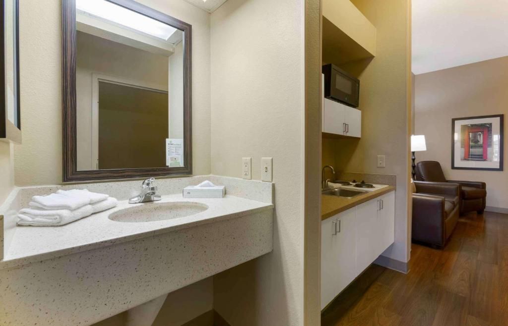 Un baño de hotel con lavamanos, espejo y televisor montado en la pared.