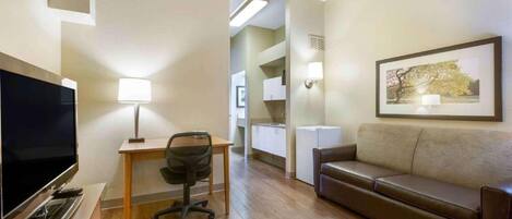 A hotel room with a flat-screen TV, a desk with a lamp, a leather sofa, and a framed picture on the wall.