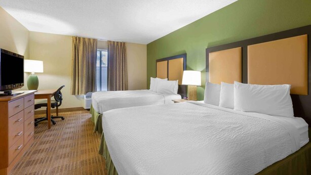 Une chambre d’hôtel avec deux lits, un bureau, une télévision et une fenêtre avec des rideaux.