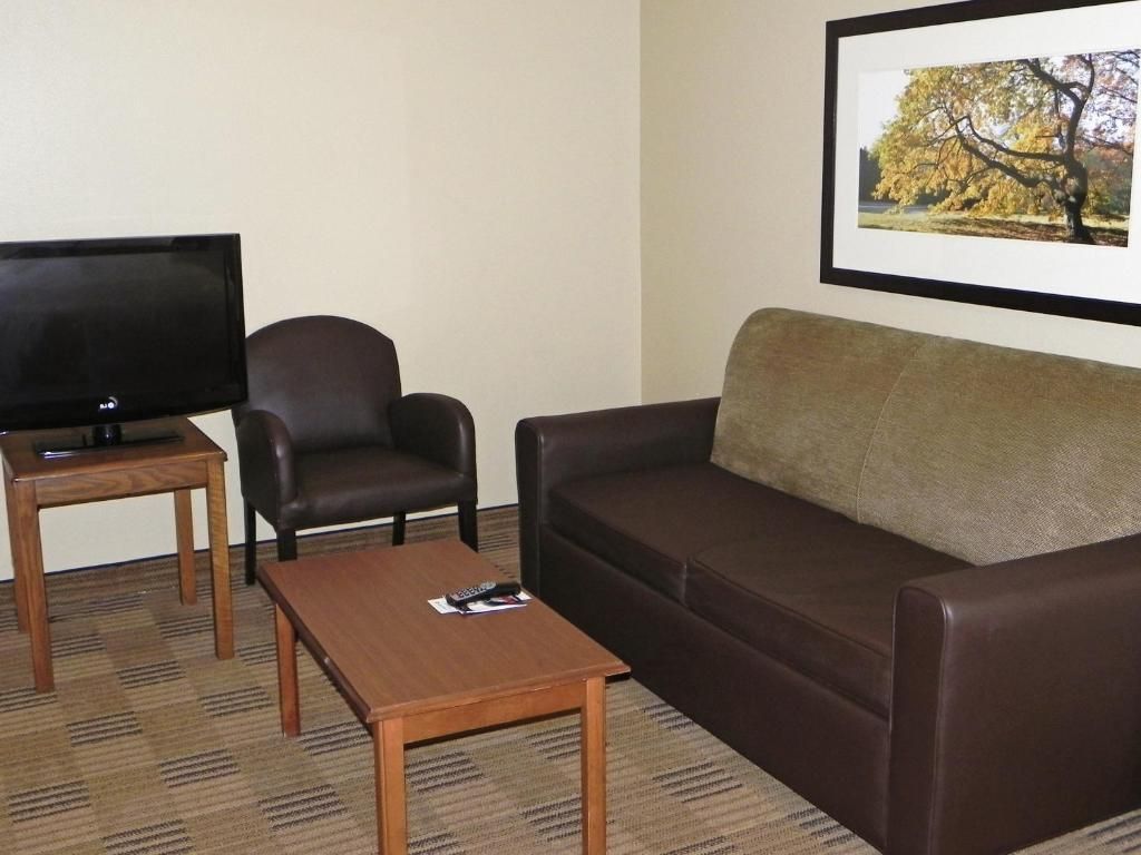A living room with a brown leather sofa, a wooden coffee table, a black armchair, and a flat-screen TV on a wooden stand.