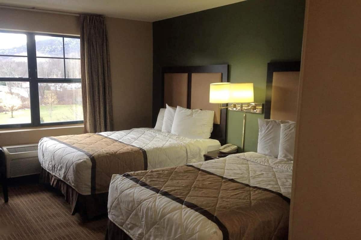 A hotel room with two beds, a window with a view, a bedside lamp, and a telephone on the nightstand.