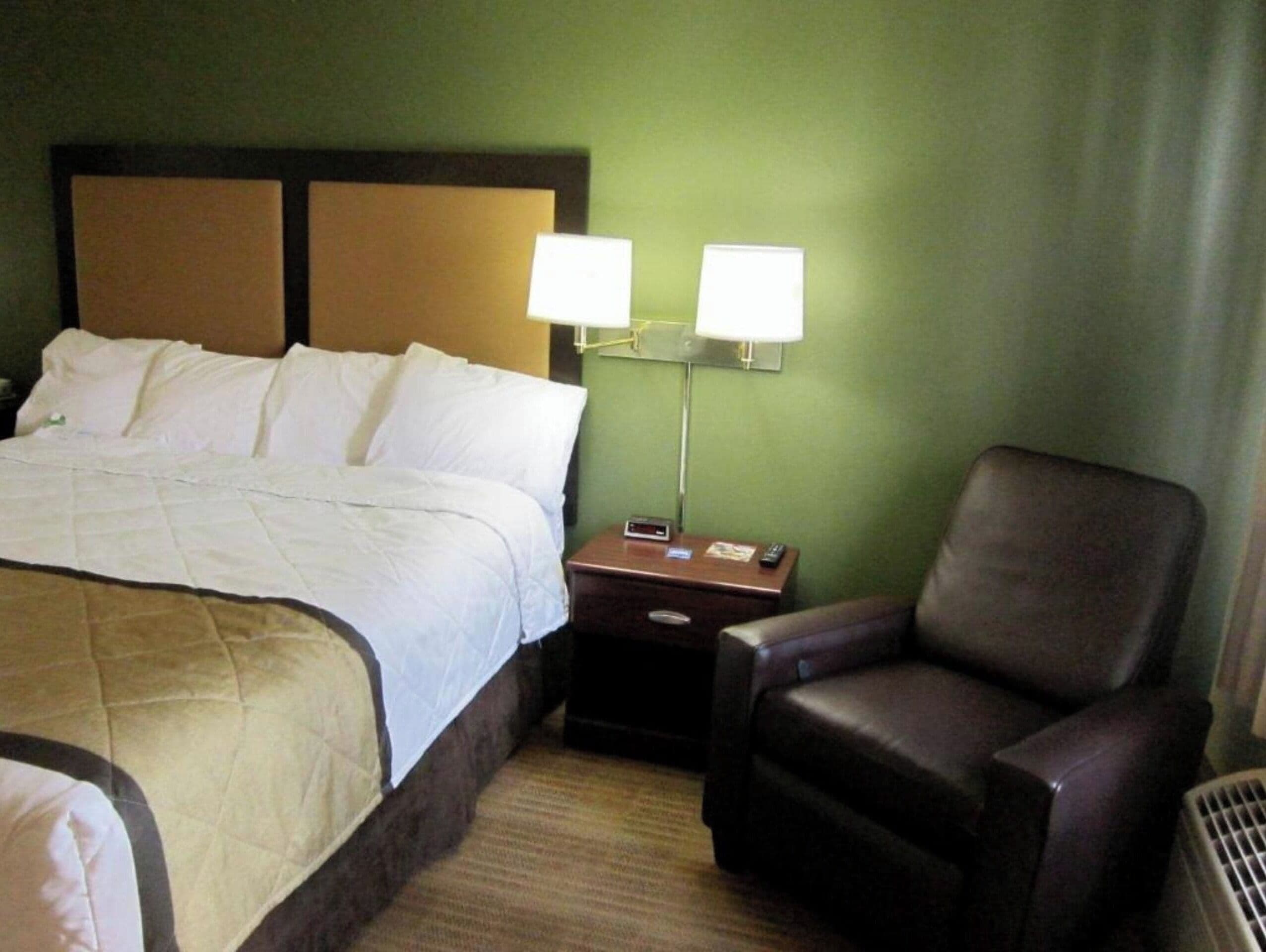 A hotel room with a bed, two bedside lamps, a chair, and a nightstand.