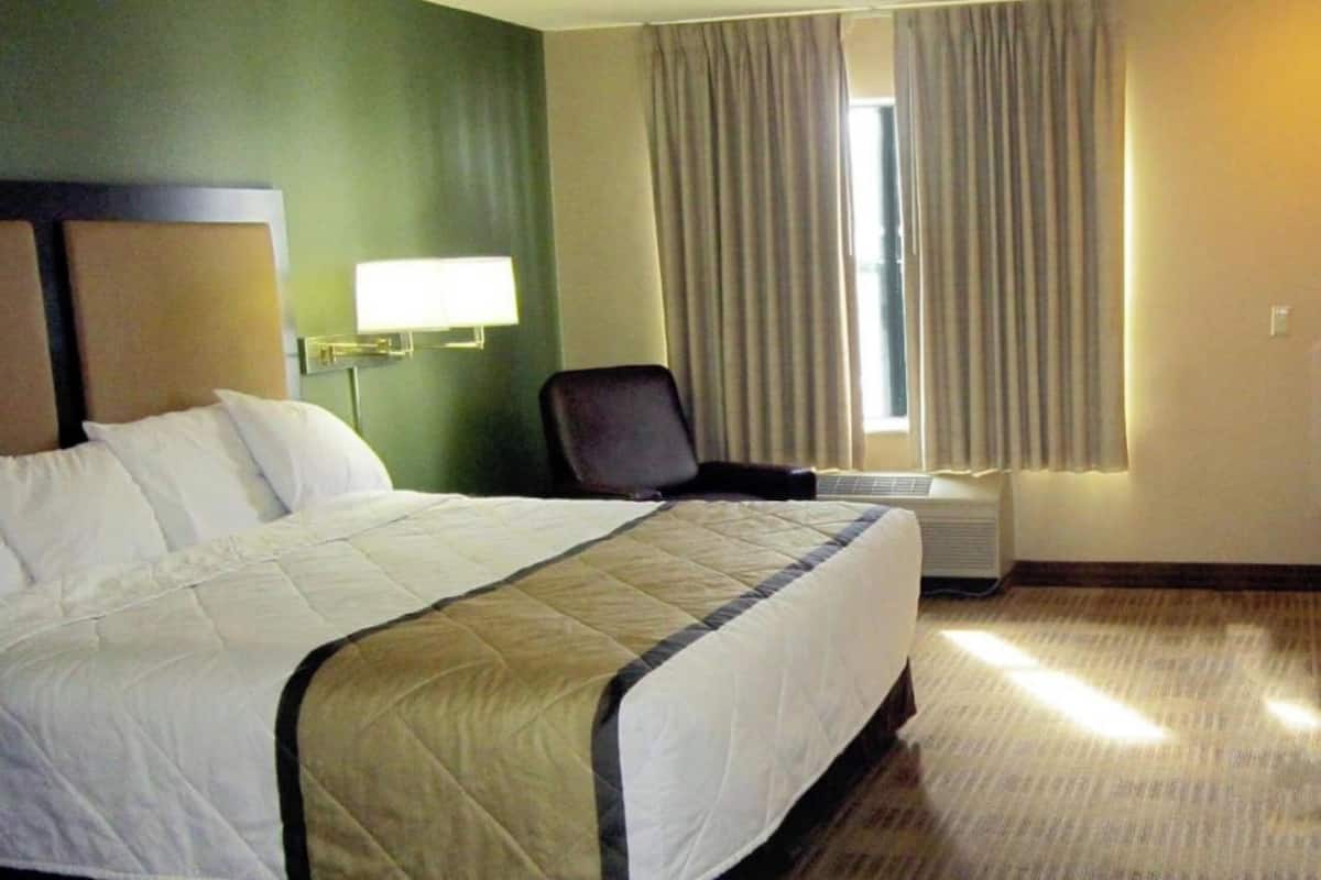A hotel room with a large bed, a chair, a lamp, and a window with curtains.