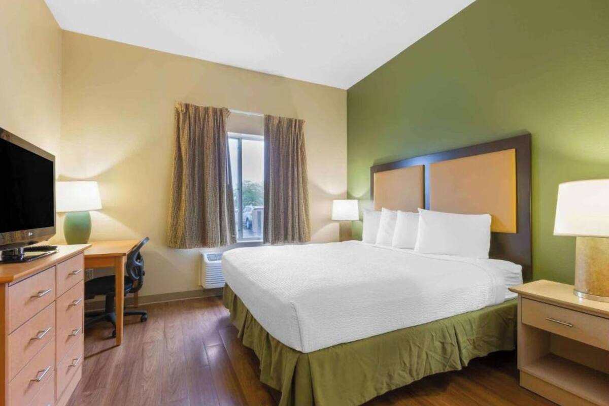 A hotel room with a bed, a desk, a television, and a window with curtains.